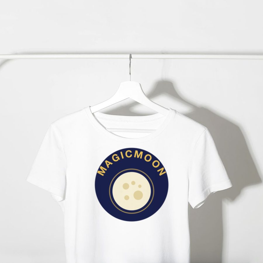 White t-shirt on a hanger with a full moon design and the word MAGICMOON curved around it printed on the chest